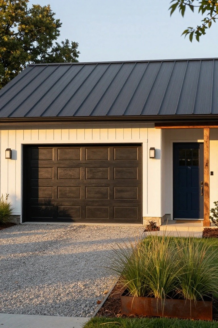 Crisp white board-and-batten garage with dark wood door and blue entry door, gravel driveway, evening light