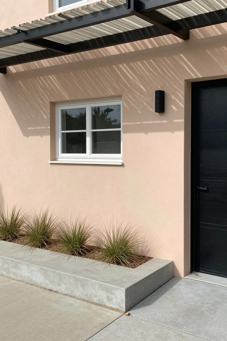 Soft warm beige stucco garage wall beside a black door, with white window and grasses in front