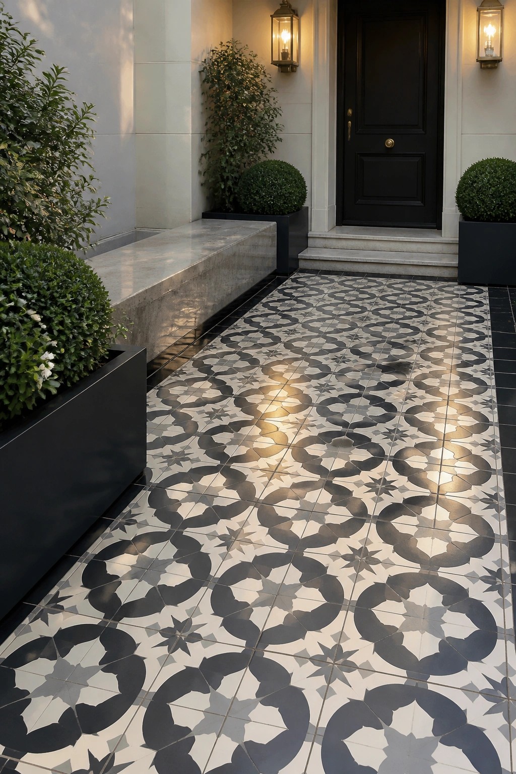 A black and white geometric patterned tile walkway leads to a black front door, with black planters holding shrubs on both sides and two wall lanterns mounted beside the door.