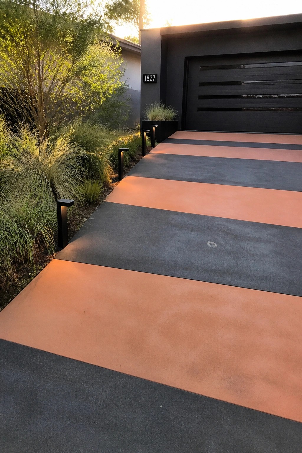 Modern striped driveway with orange and gray concrete leading to black garage at sunset.
