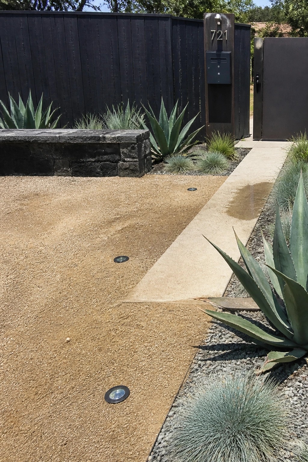 Modern entrance with agave plants, concrete path, gravel, and black fence with 721 sign.
