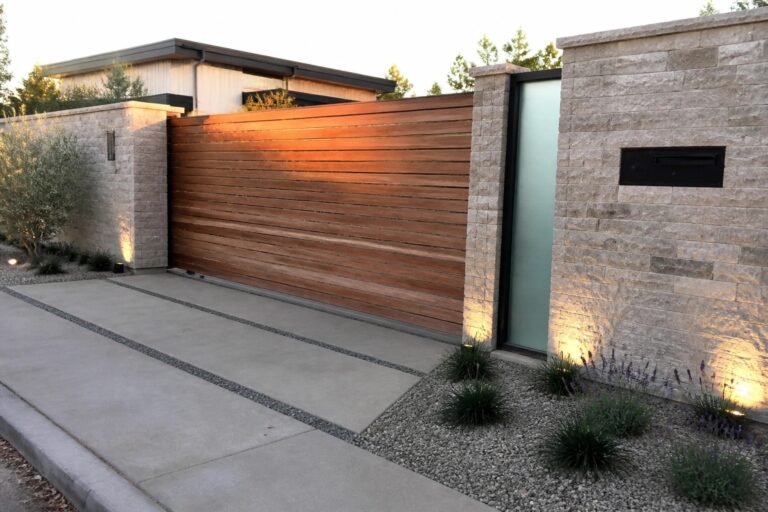 19 Practical Main Gate Design Ideas That Balance Beauty and Function A modern wooden gate with horizontal slats set between stone pillars, next to a frosted glass side door with the number 3724 on a concrete driveway.
