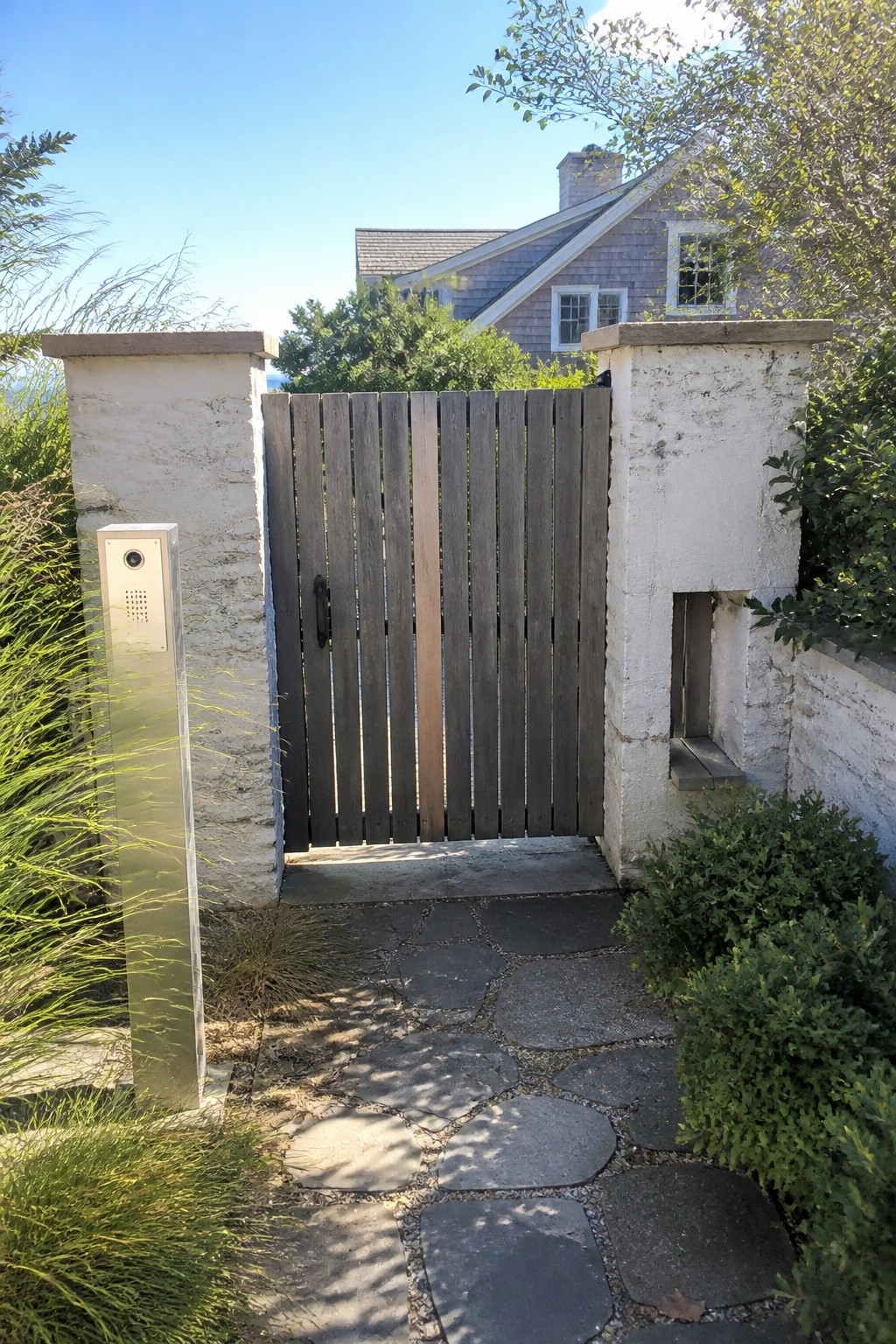 Wooden gate between white stone pillars on path to gray shingled house.
