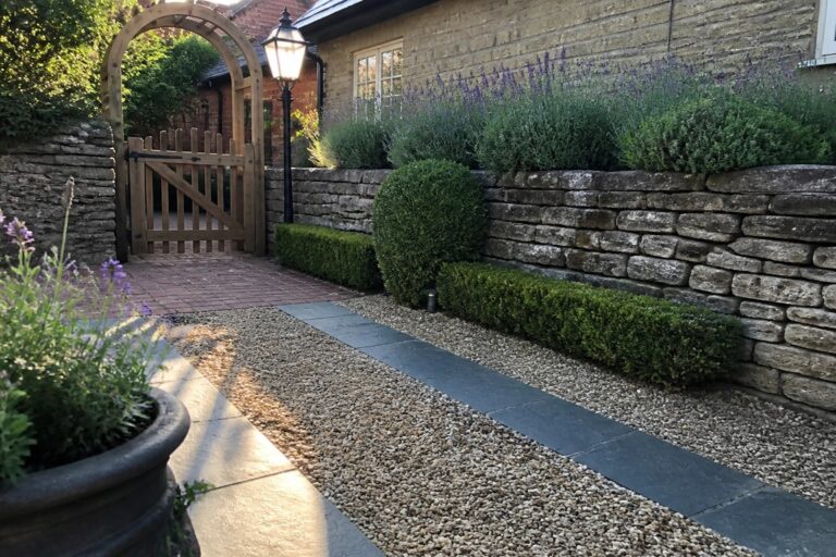 19 Clever Small Gravel Driveway Ideas That Maximize Tight Spaces Stone slab path with gravel, round shrubs, lavender, lit lamppost, and arched wooden gate.