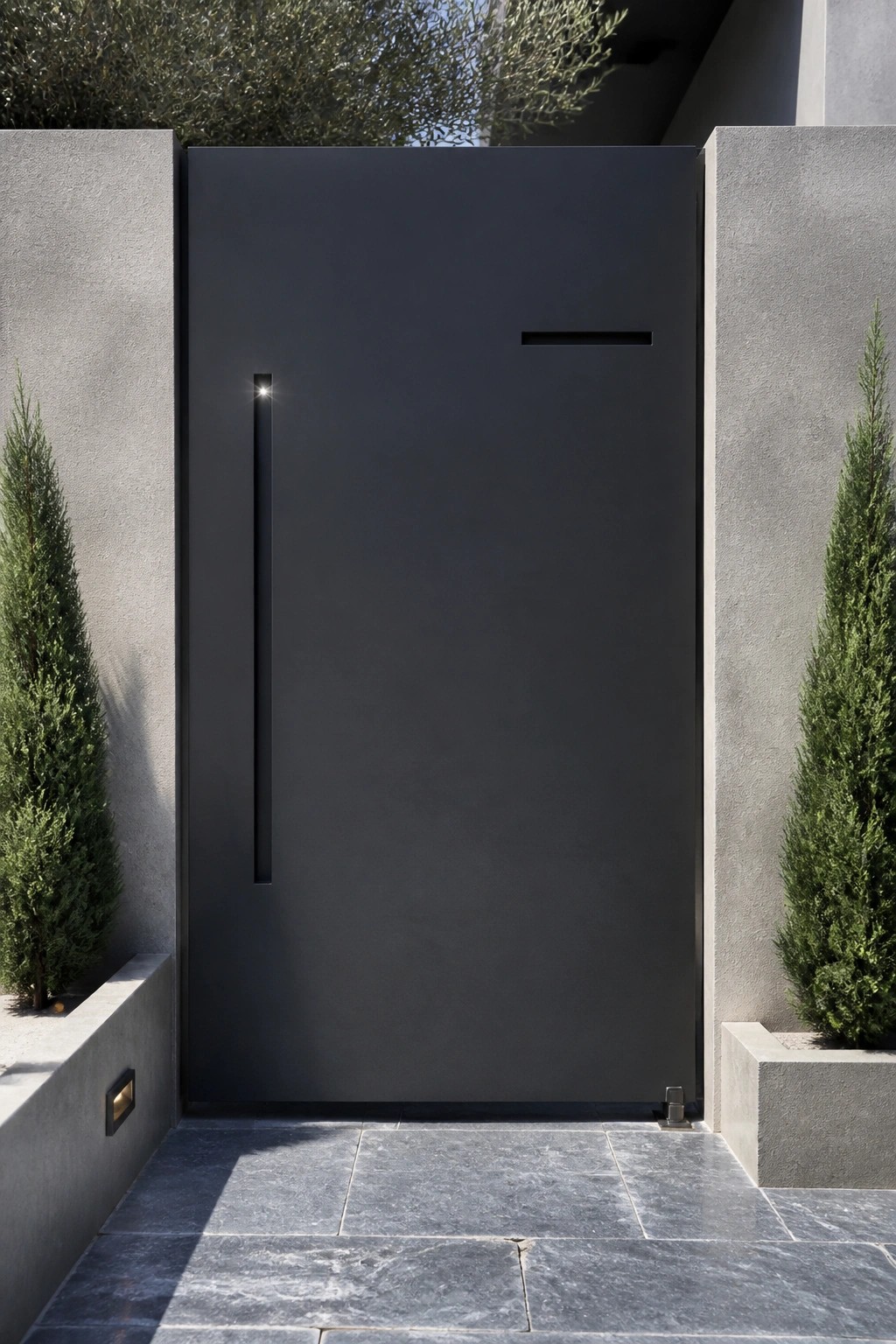 A dark gray steel gate with a vertical recessed handle and small horizontal slot, set between concrete walls on a paved stone entry.