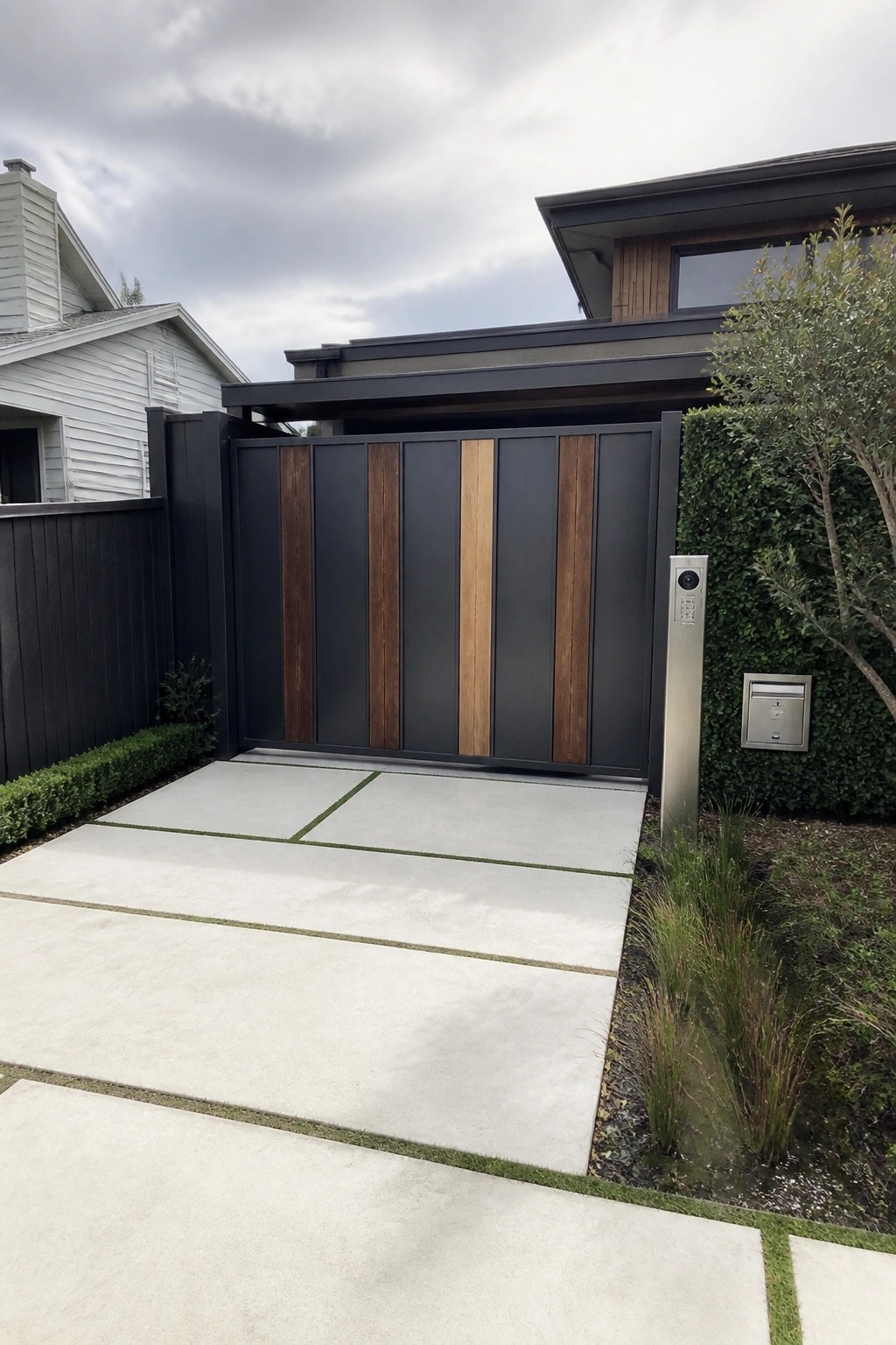 Modern black gate with vertical wood panels at end of concrete driveway