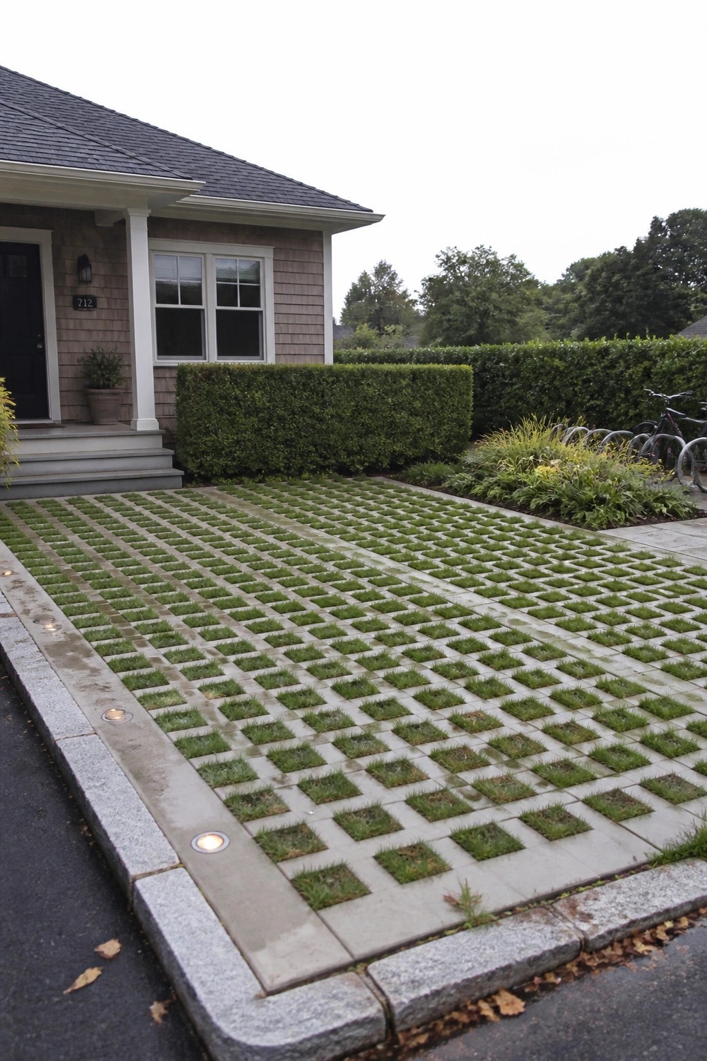 A driveway covered in light gray grid pavers with grass growing in each square, bordered by granite edging in front of a shingled house.