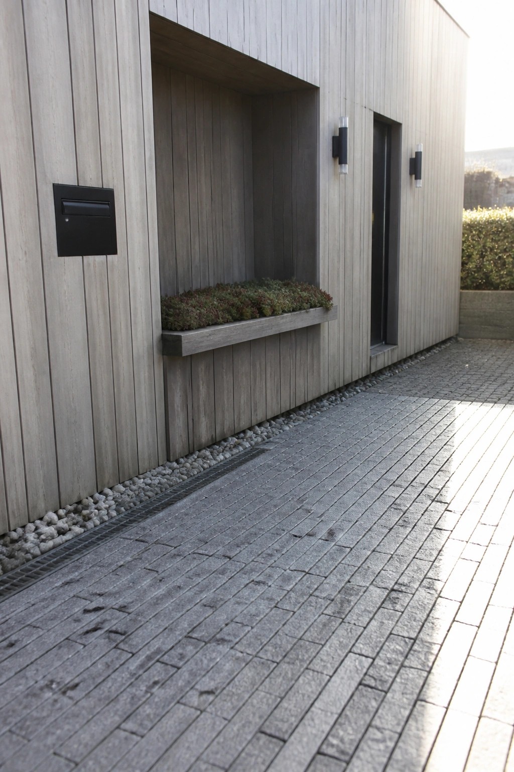 Modern light wood facade with black mailbox, recessed planter, and dark door