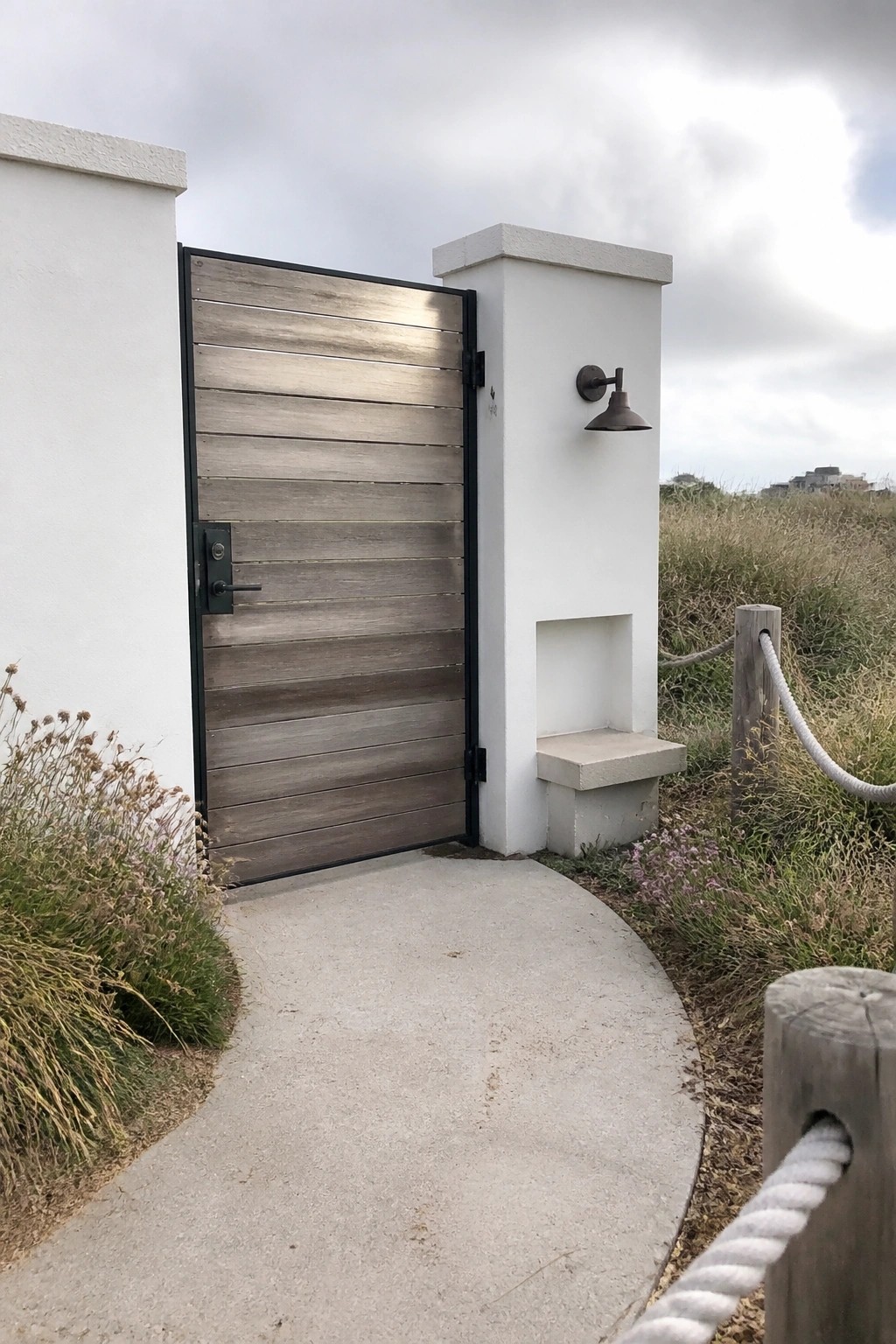 Horizontal wood gate ajar beside white pillar with sconce on coastal path