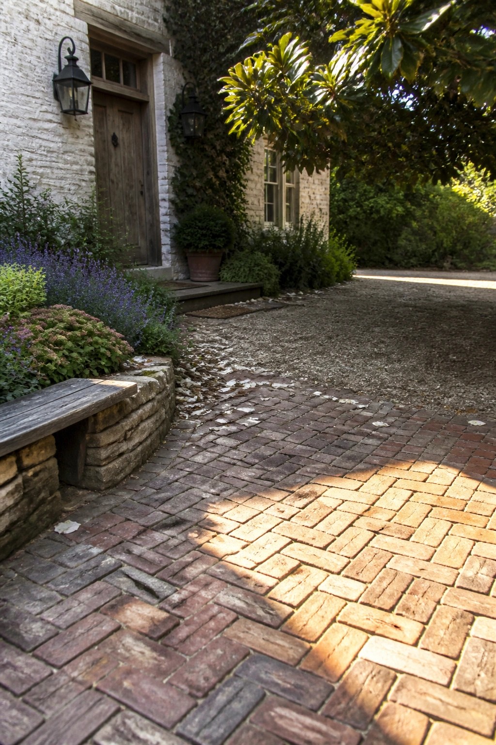 Sunlit brick pathway leading to ivy-covered house with wooden door and plants