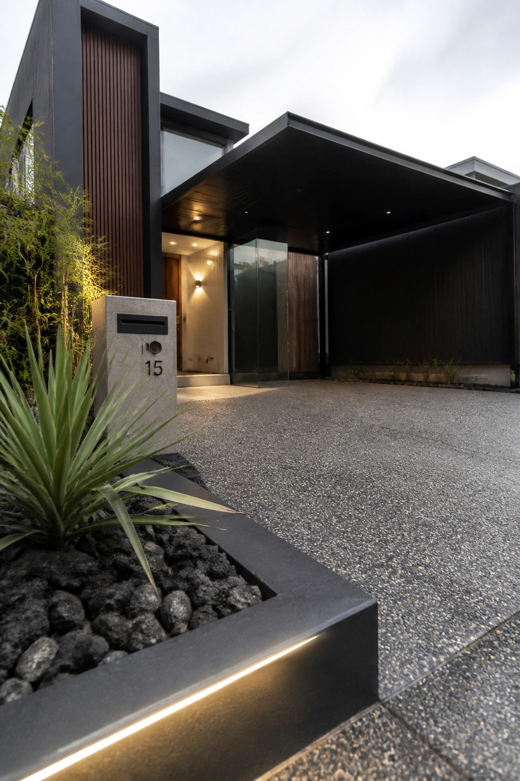 Modern black house entrance with mailbox 15, gravel drive and lit rock planter