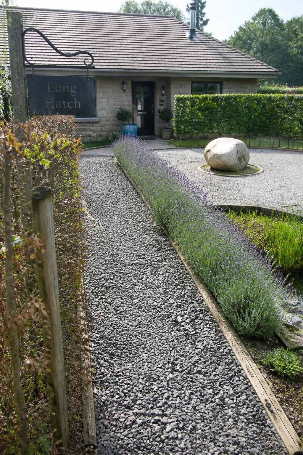 Gravel path lined with lavender leads to stone house with Long Hatch sign and boulder