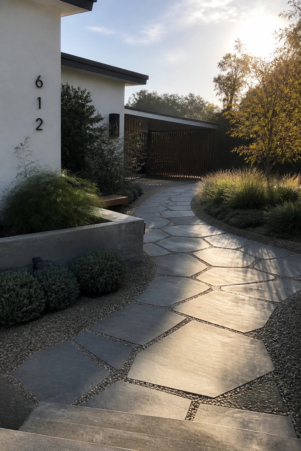 A curved driveway made of irregular gray stone pavers leads toward a modern white house with gravel borders and low landscaping.