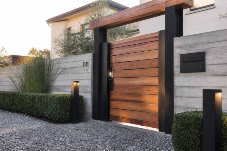 20 Striking Wooden Main Gate Designs That Bring Warm Natural Appeal A wooden gate with horizontal slats framed in black metal, positioned between concrete walls with pathway lights on either side.