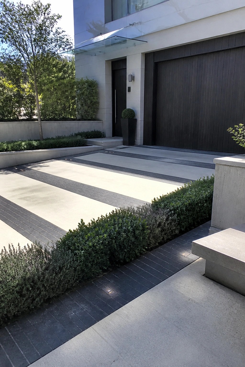 Modern home with dark garage, black door, striped driveway, and green hedges.
