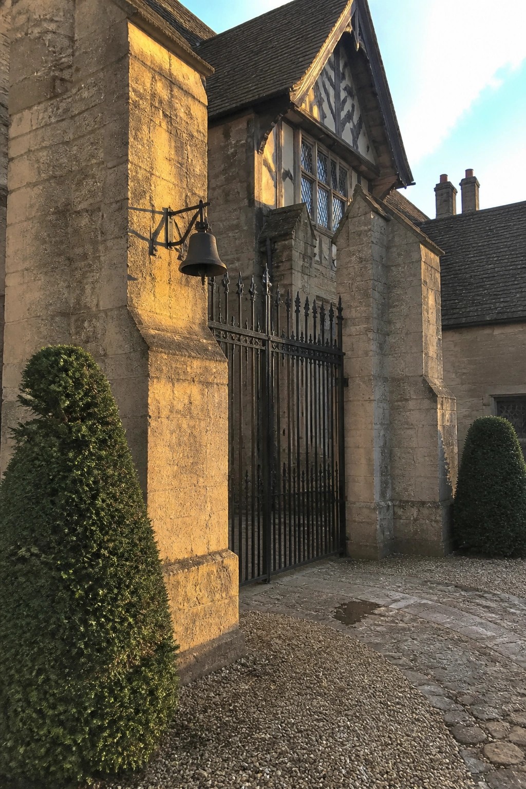 Stone gateway with black iron gate, bell on wall and green topiary bushes