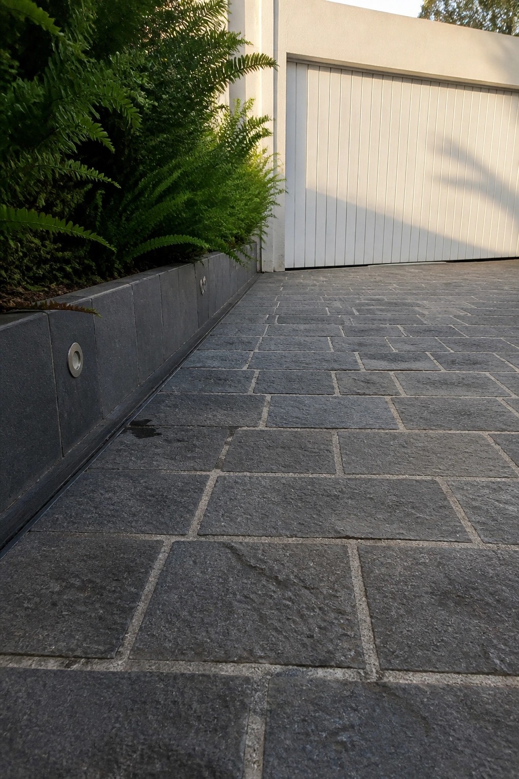Dark stone pavers beside low wall with ferns and white garage door