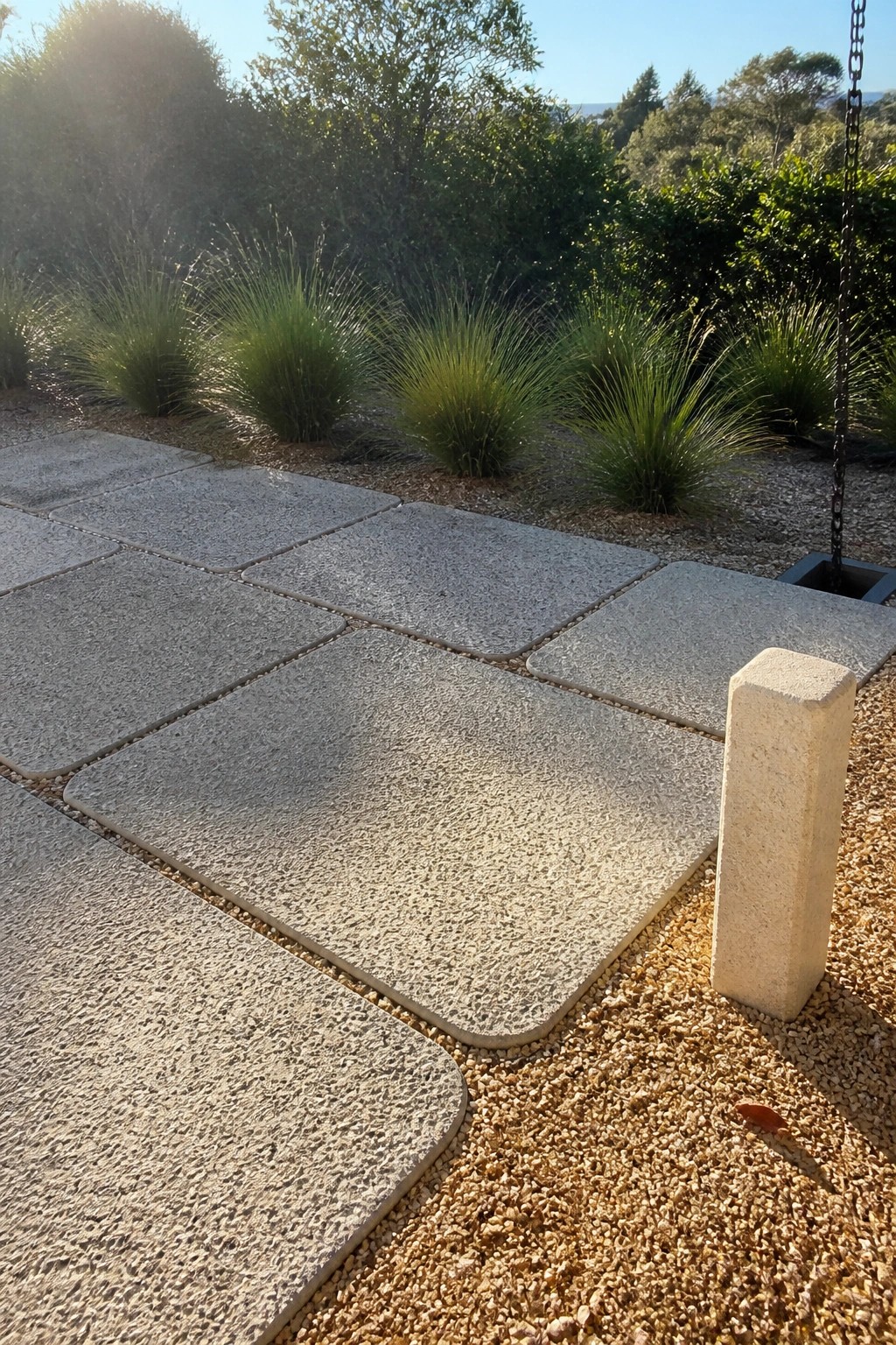Sunlit stone paver path on gravel beside white bollard and green grasses