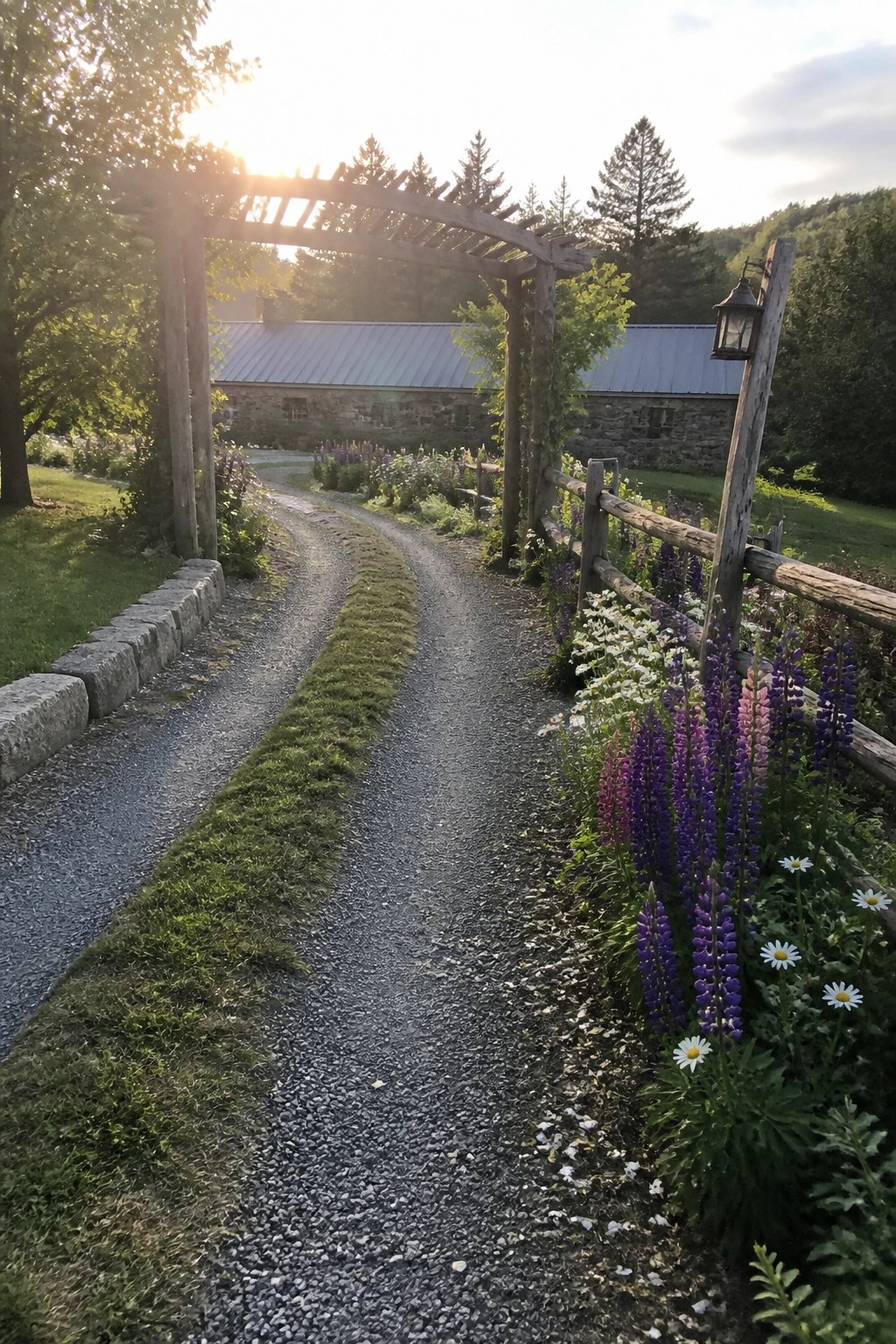 A gravel driveway curves past a wooden fence and arch lined with purple lupines and white daisies, leading toward a stone building.