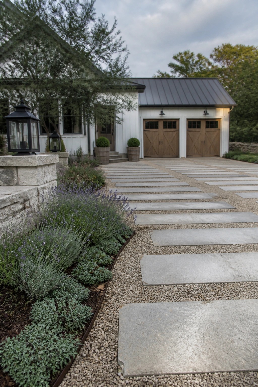 White house with wooden garage doors and lavender-lined stone pathway in gravel.
