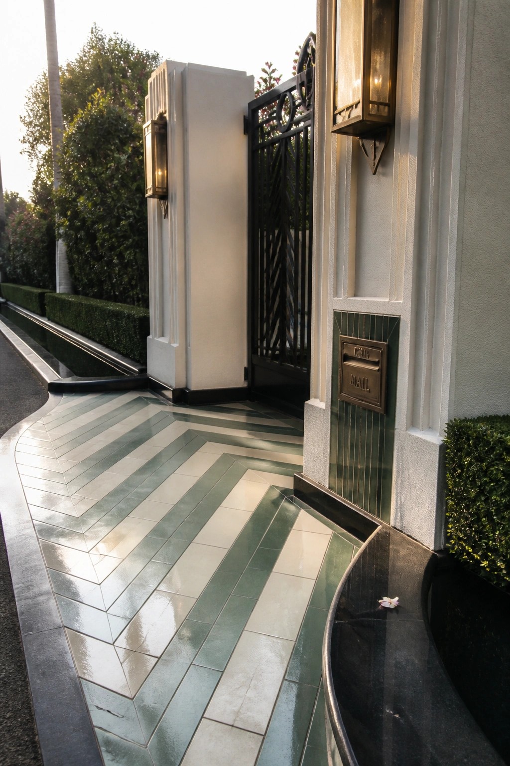 Elegant entrance with black ornate gate, green-white striped tiles, and wall sconces