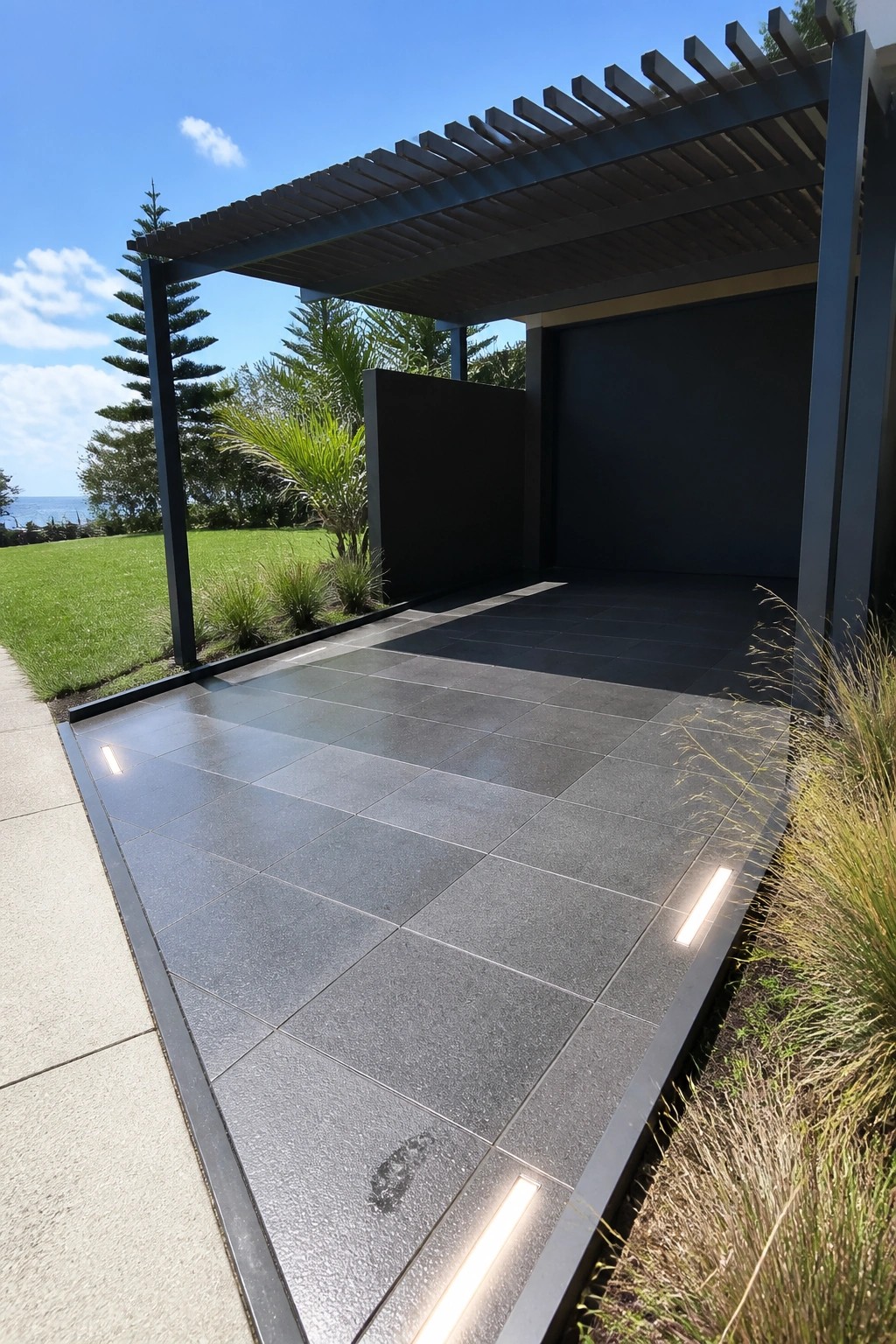 Modern dark-tiled carport with slatted roof, recessed lights, and ocean view.