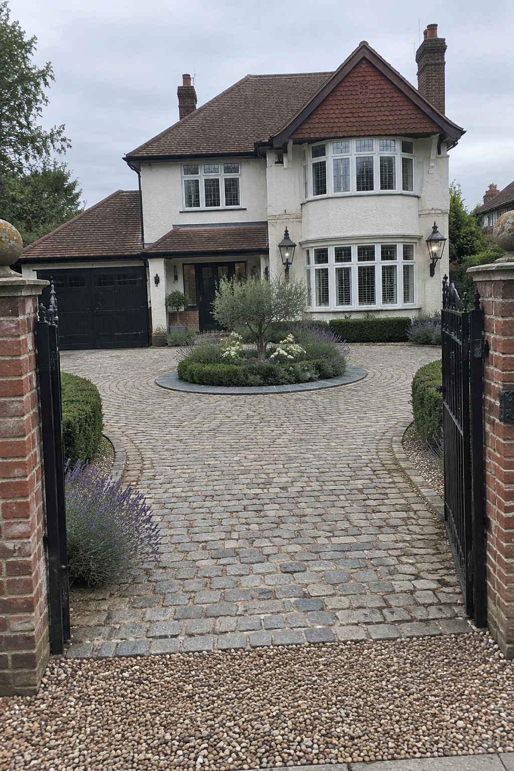 White house with red roof behind cobblestone driveway and open black gates