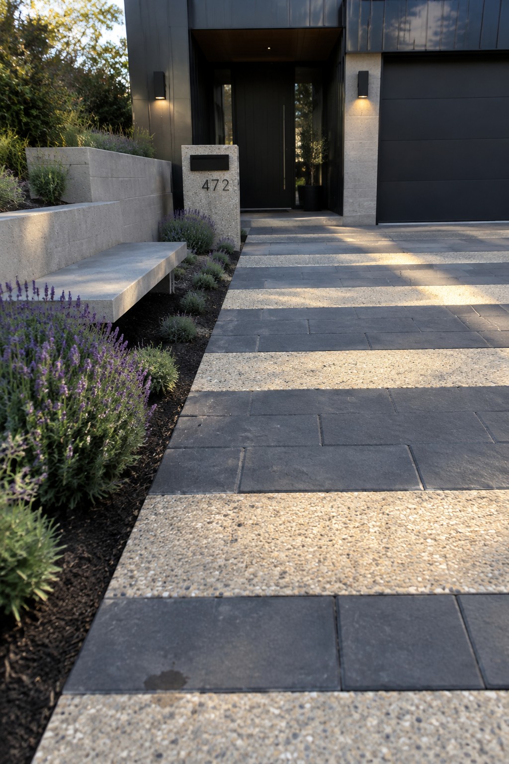 A modern home entrance showing a driveway made of alternating dark gray pavers and light speckled concrete bands, with lavender plants along the left side and a concrete mailbox marked 472.