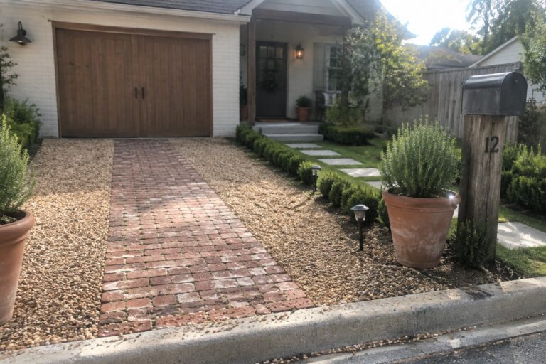 18 Affordable Small Driveway Ideas Using Budget-Friendly Landscaping and Surfaces Brick house with wooden garage, brick path, gravel beds, shrubs, and mailbox post