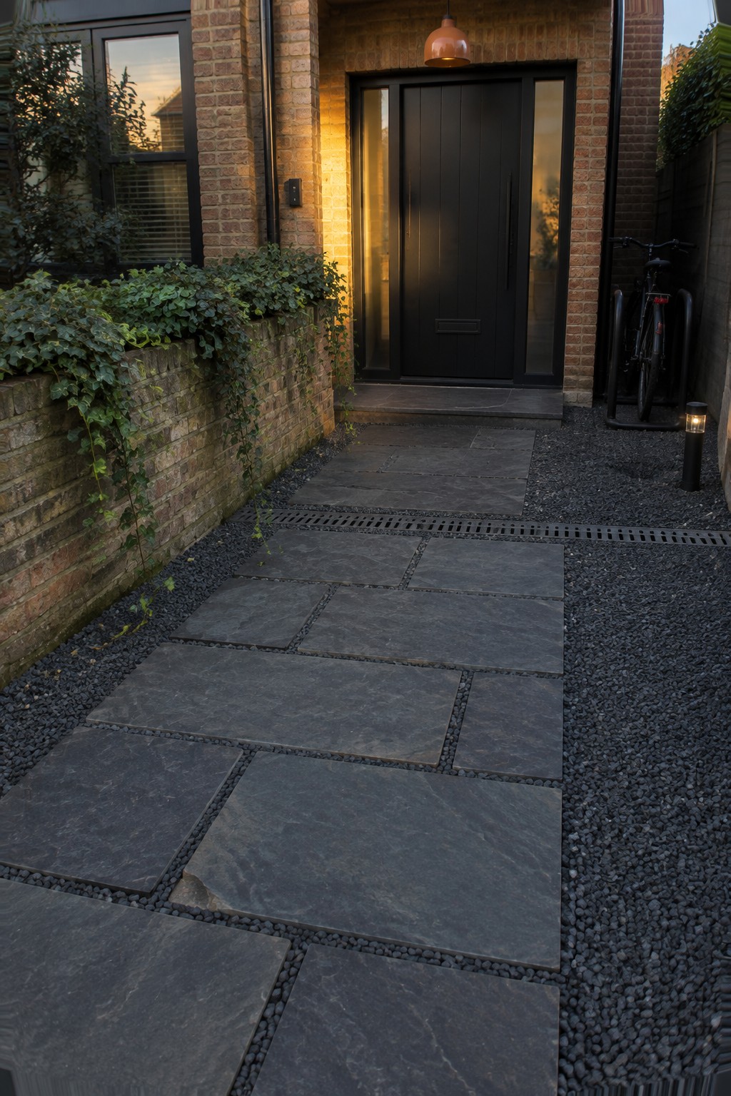 Modern brick home entrance with black door, stone path, ivy and bicycle