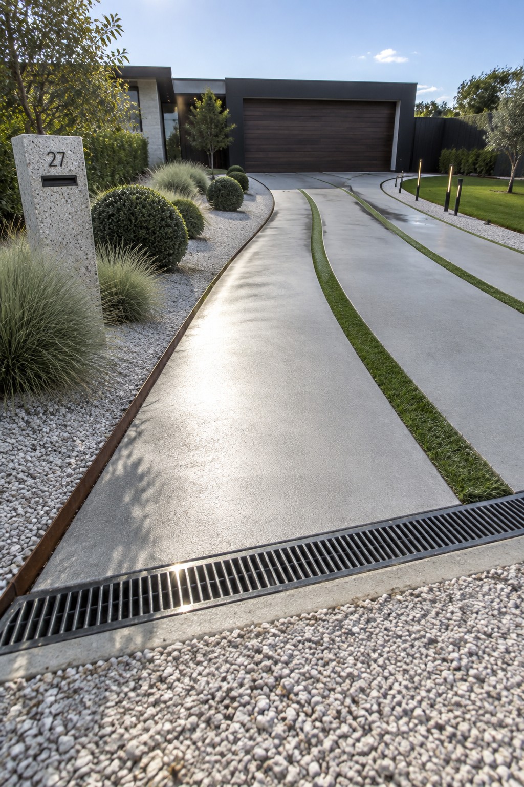 A modern house exterior with a curved concrete driveway bordered by grass strips and gravel beds, including a stone address pillar marked 27.