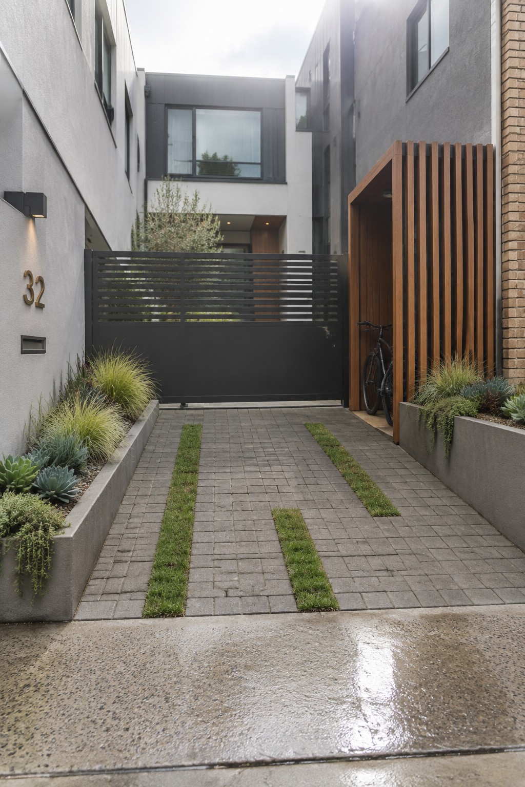 Modern courtyard with black gate, bike in wooden slats, concrete planters, and grass-paved path.